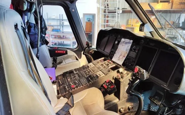 The cockpit of a helicopter shows the instrument panel, controls, and pilot's seat.