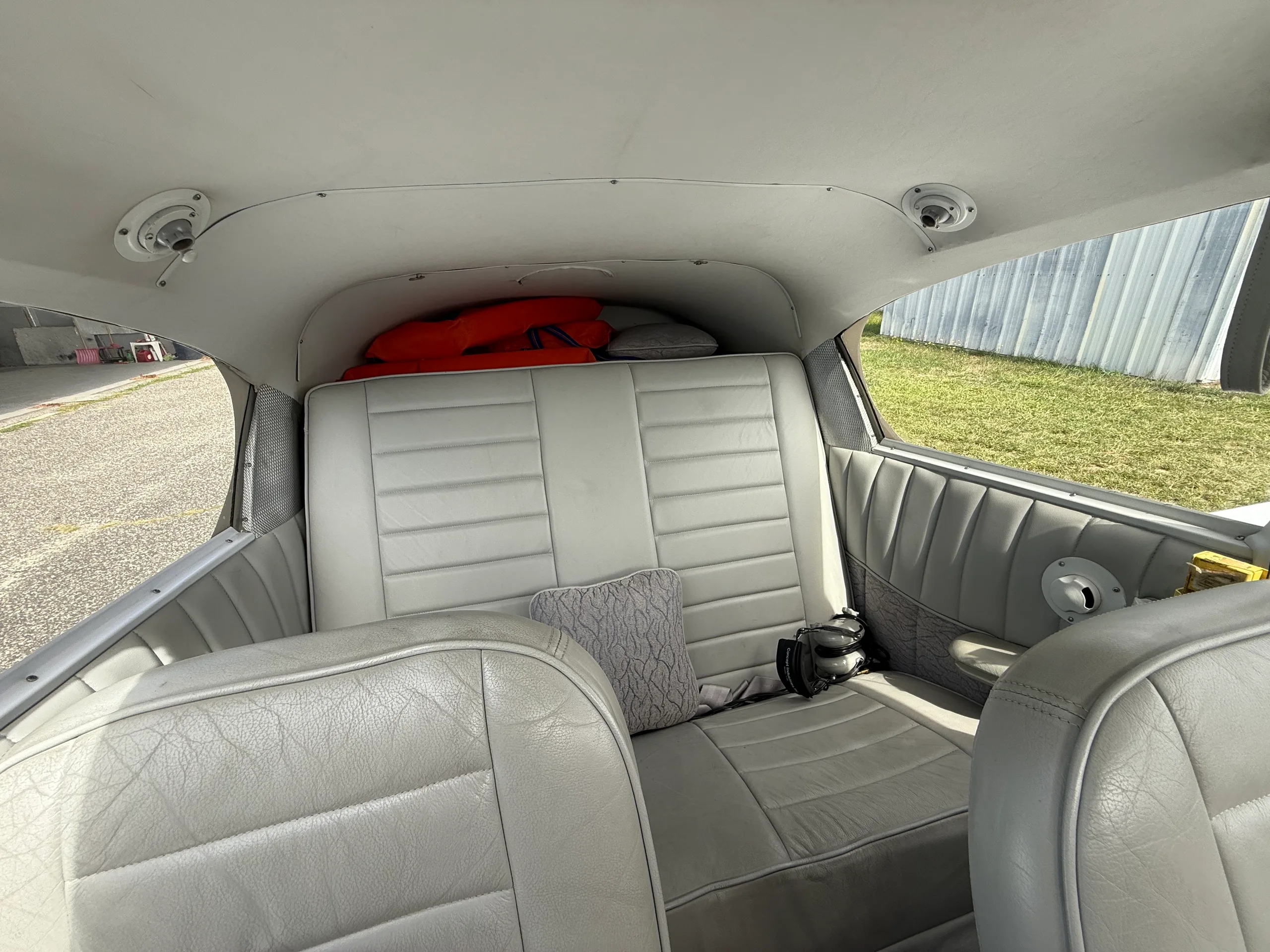View of the light gray rear cabin seats of a small aircraft, with orange life vests visible in the baggage area.
