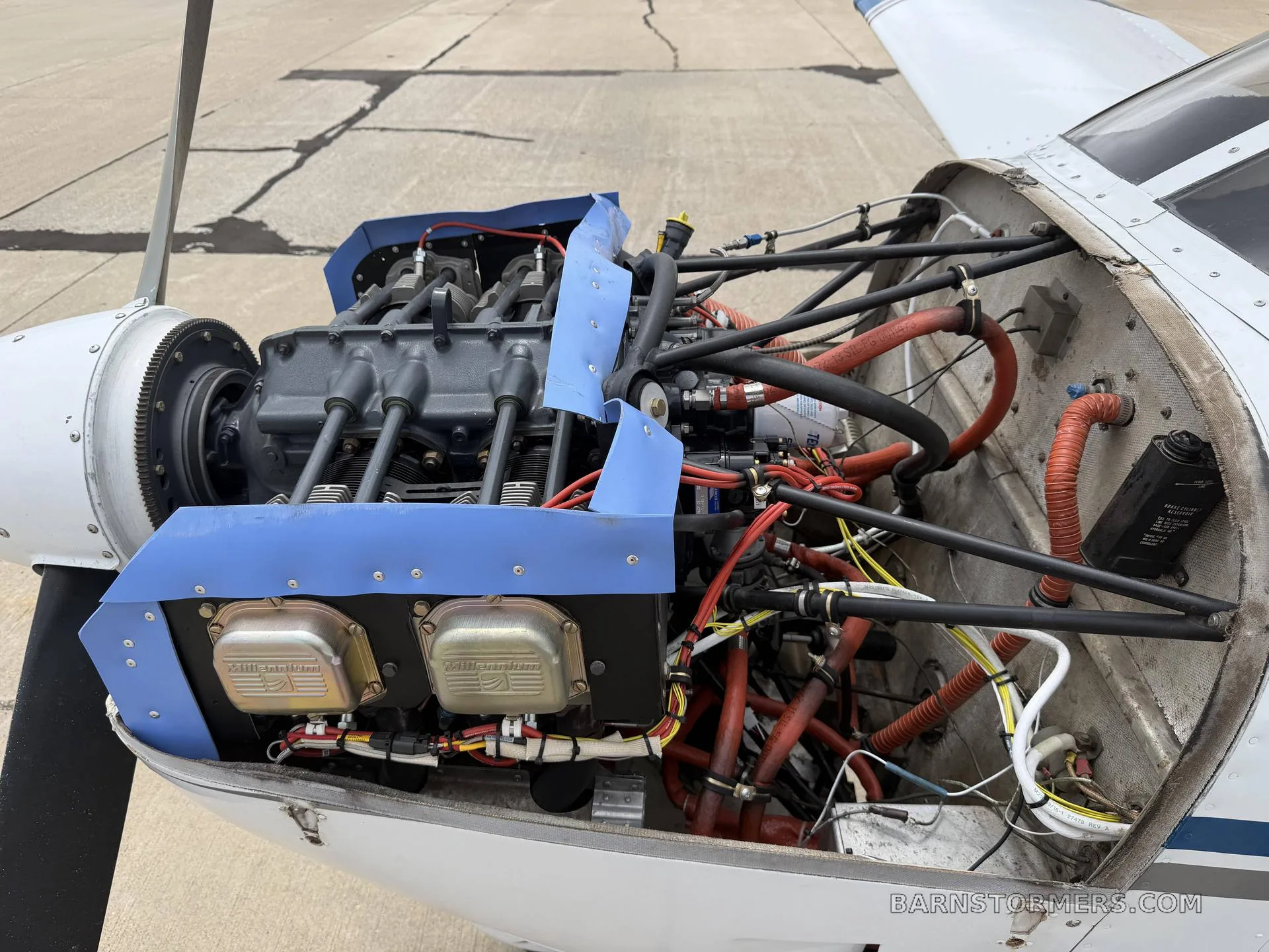 The exposed engine bay of a Piper Cherokee, showing the engine, wiring, and hoses with the cowling removed.