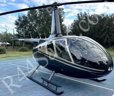 A dark blue and gold Robinson R66 Turbine helicopter is parked on a paved surface under a cloudy sky.