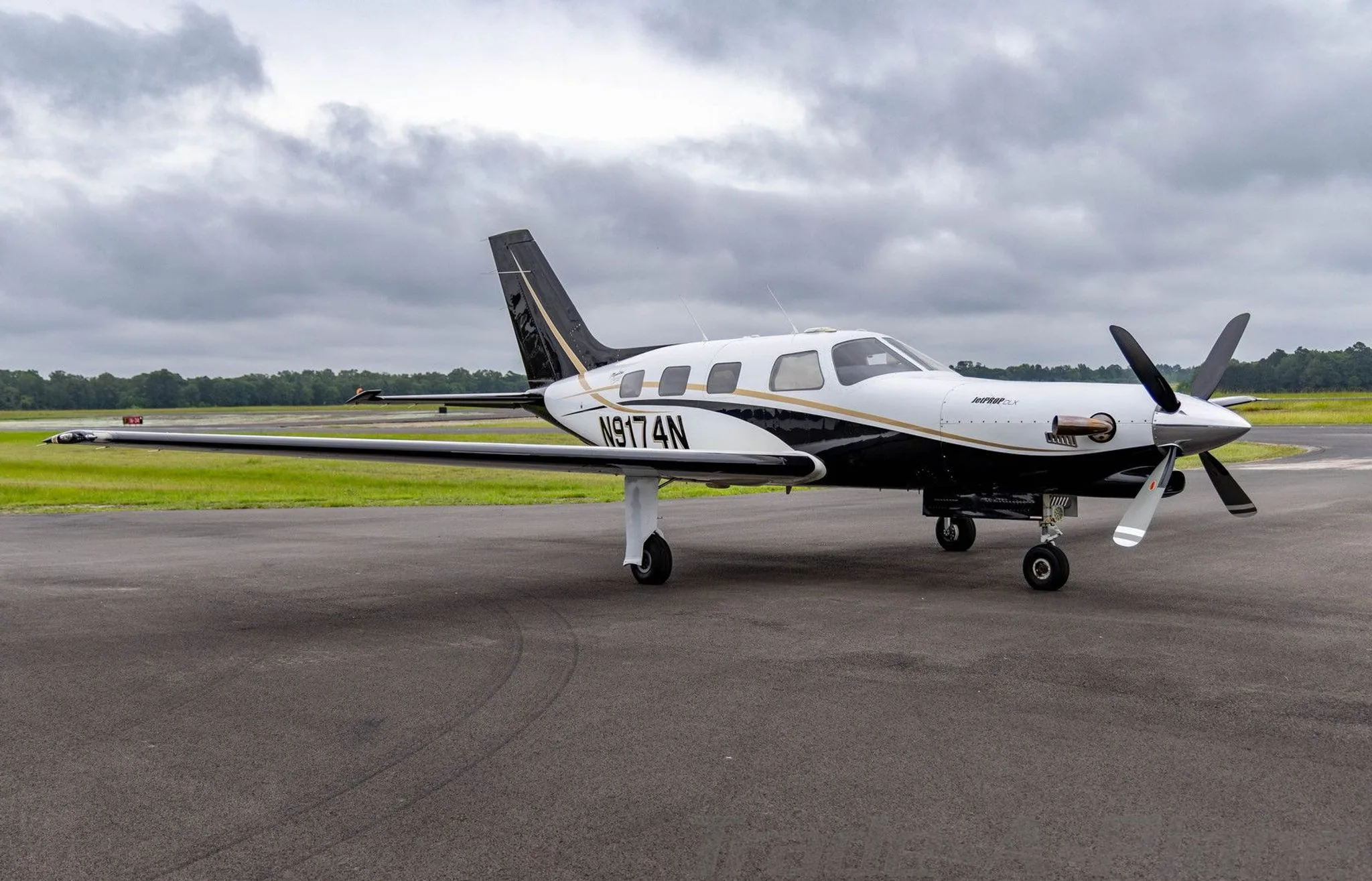 A white and black Piper Malibu Mirage (JetPROP DLX) N9174N with gold accents parked on a tarmac, viewed from the front-right.