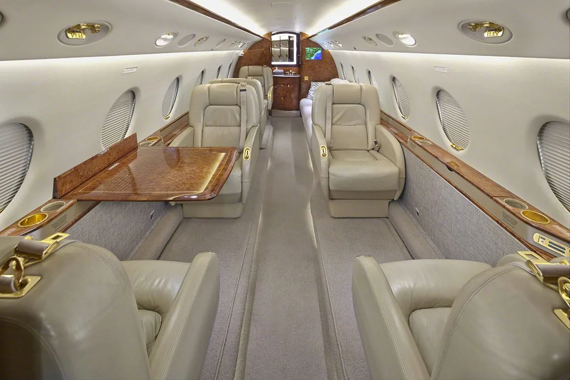 The luxurious interior cabin of a private jet with beige leather seats and polished wood tables.