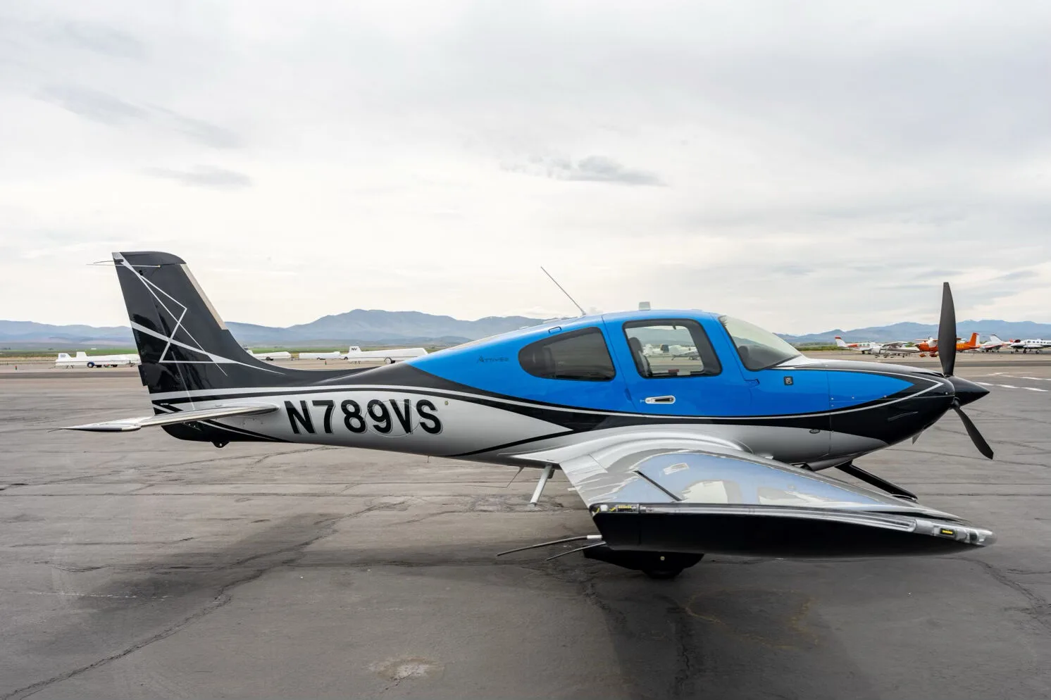 Side view of a black, blue, and silver single-engine aircraft with registration N789VS on an airfield, showing the wing.