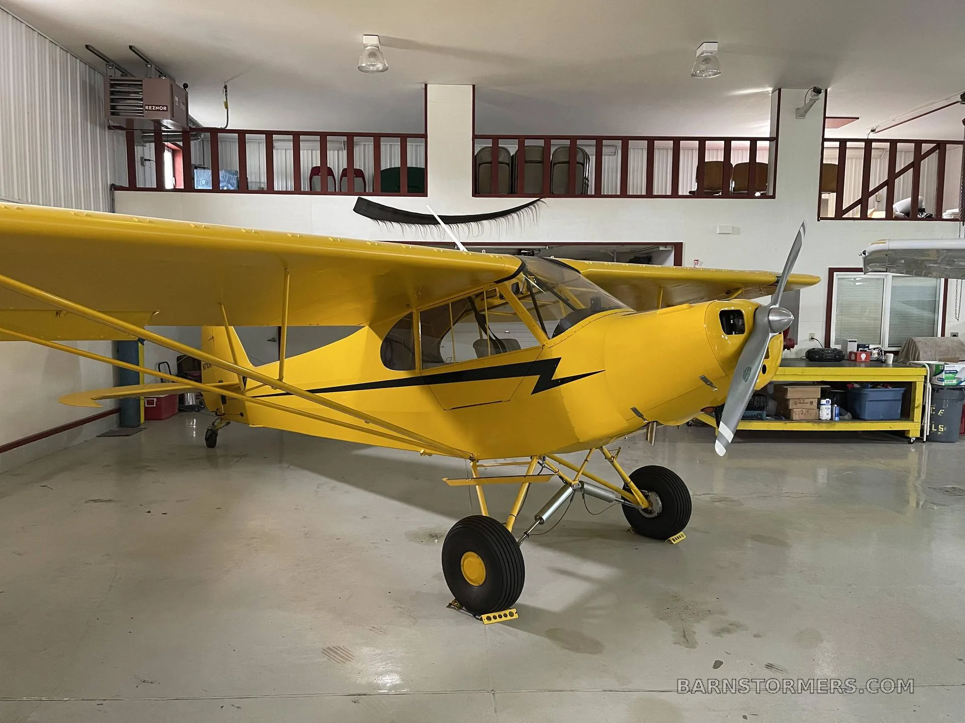A yellow single-engine aircraft, possibly a Piper Cub, is parked inside a hangar.