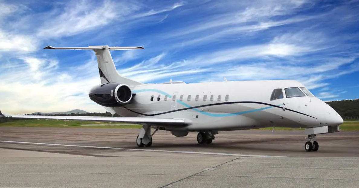 A white Embraer Legacy 600 series business jet with blue and black livery is parked on an airport tarmac under a blue sky.