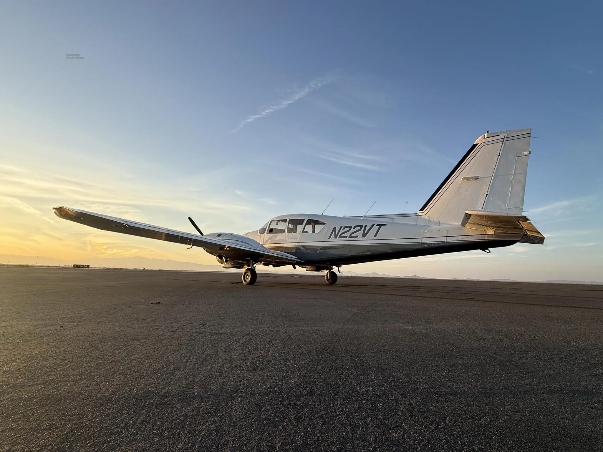 A silver and white single-engine aircraft, N22VT, is parked on an airfield at sunset.