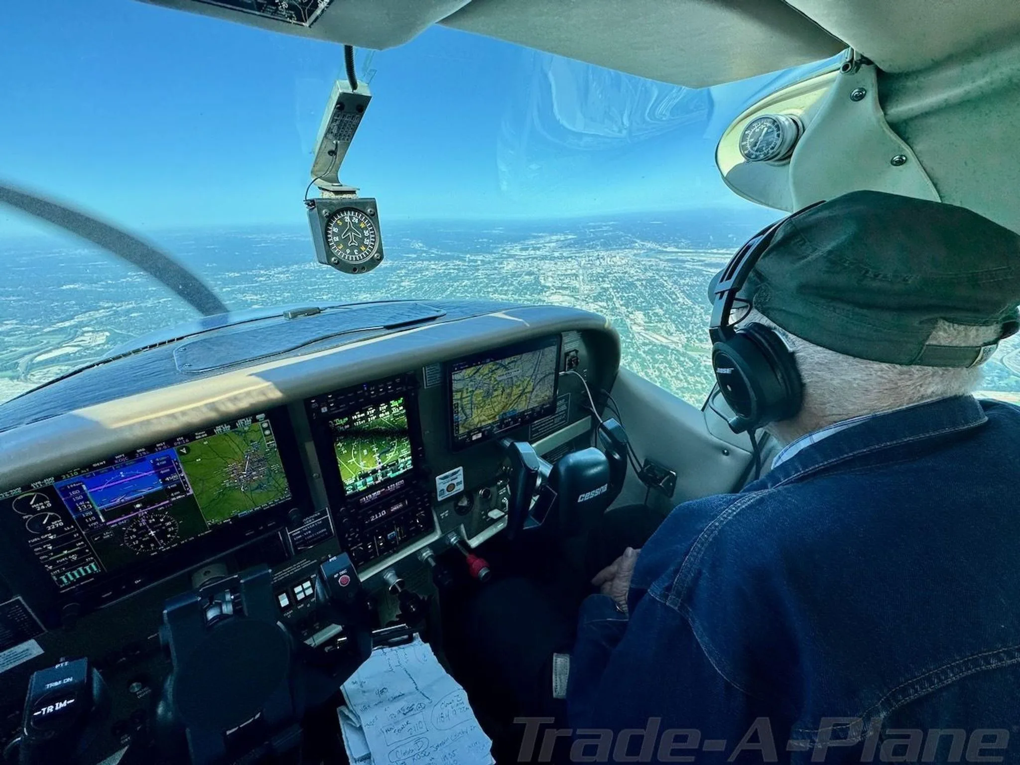 A pilot in the cockpit of Cessna N2612Q flying over a city with a clear blue sky.