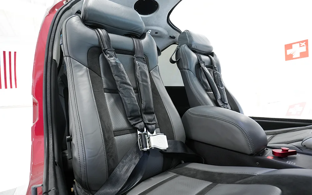 The gray and black leather front seats of a Cirrus SR22 aircraft, showing the seatbelts and armrest.