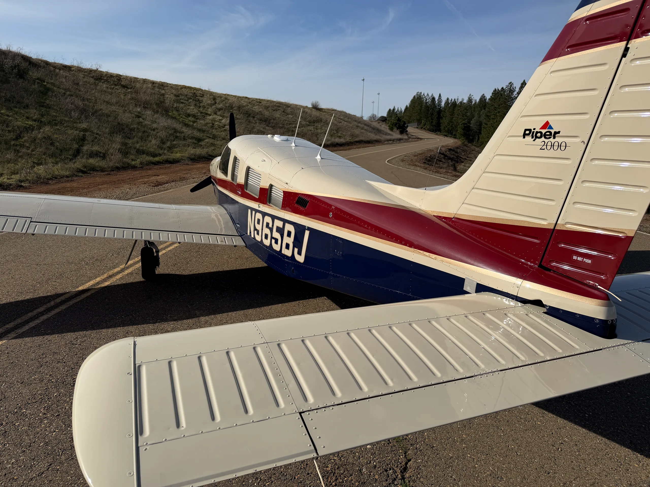 A rear view of the Piper Saratoga II TC aircraft, highlighting the tail with 'Piper 2000' logo and registration N965BJ.