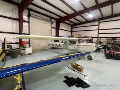 A white Cessna 150/152 type aircraft with registration N10946 is parked in a hangar, viewed from the left side.