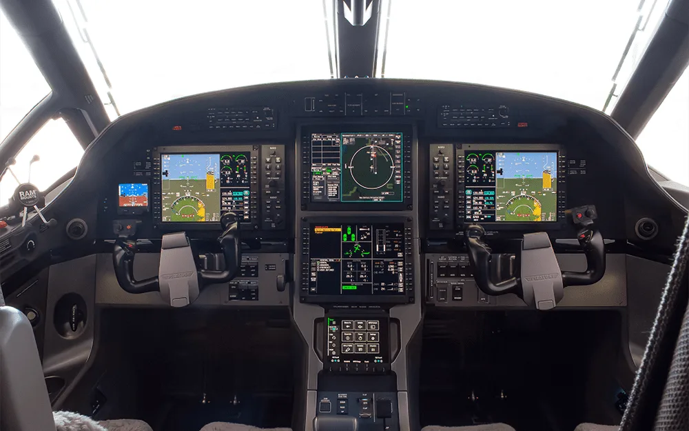 The modern glass cockpit of a Pilatus PC-12 aircraft with multiple large display screens and control yokes.
