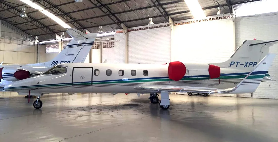 A white Learjet with green and blue stripes and red engine covers parked in a hangar.