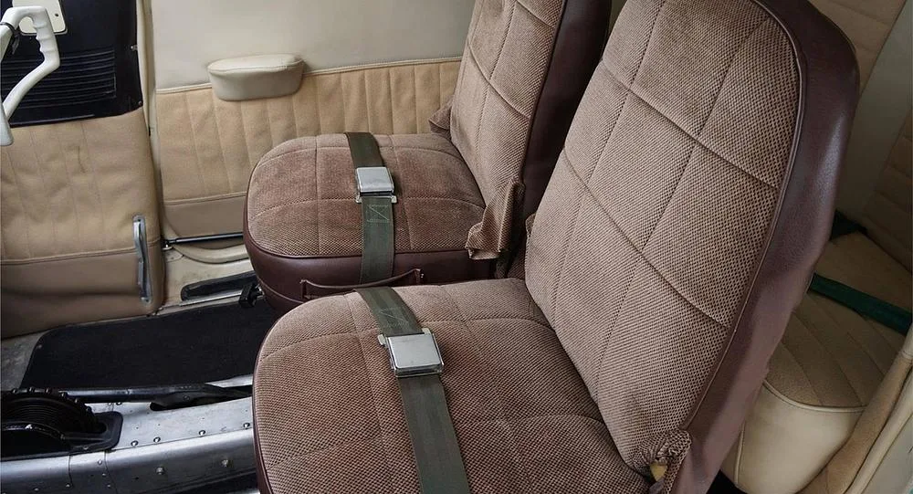 A close-up view of the two front brown and tan fabric seats in a small aircraft's interior.