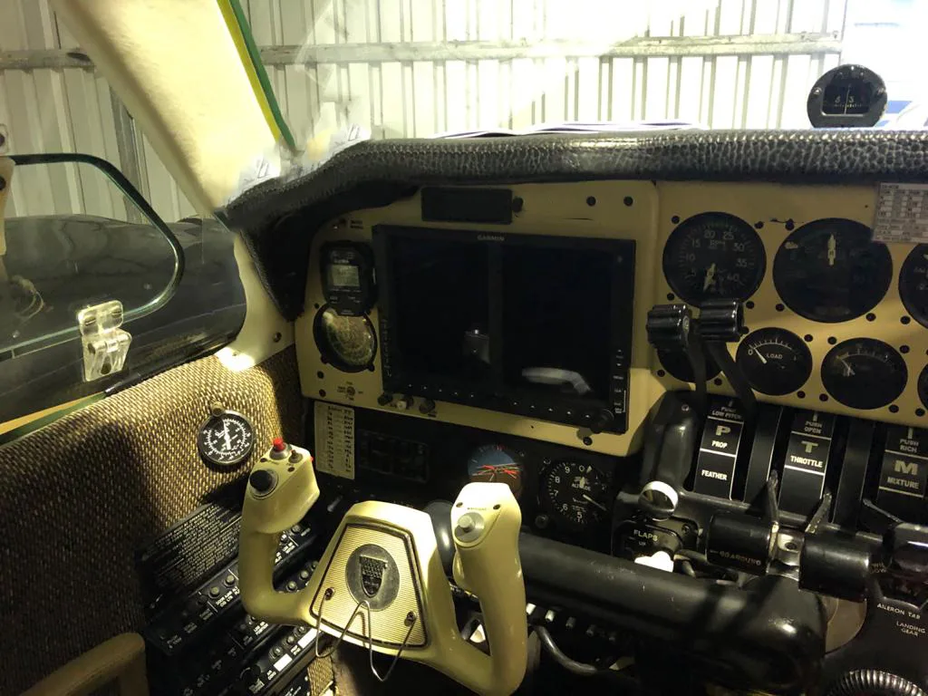 The cockpit of an aircraft, featuring a modern Garmin display, analog gauges, and dual control yokes.