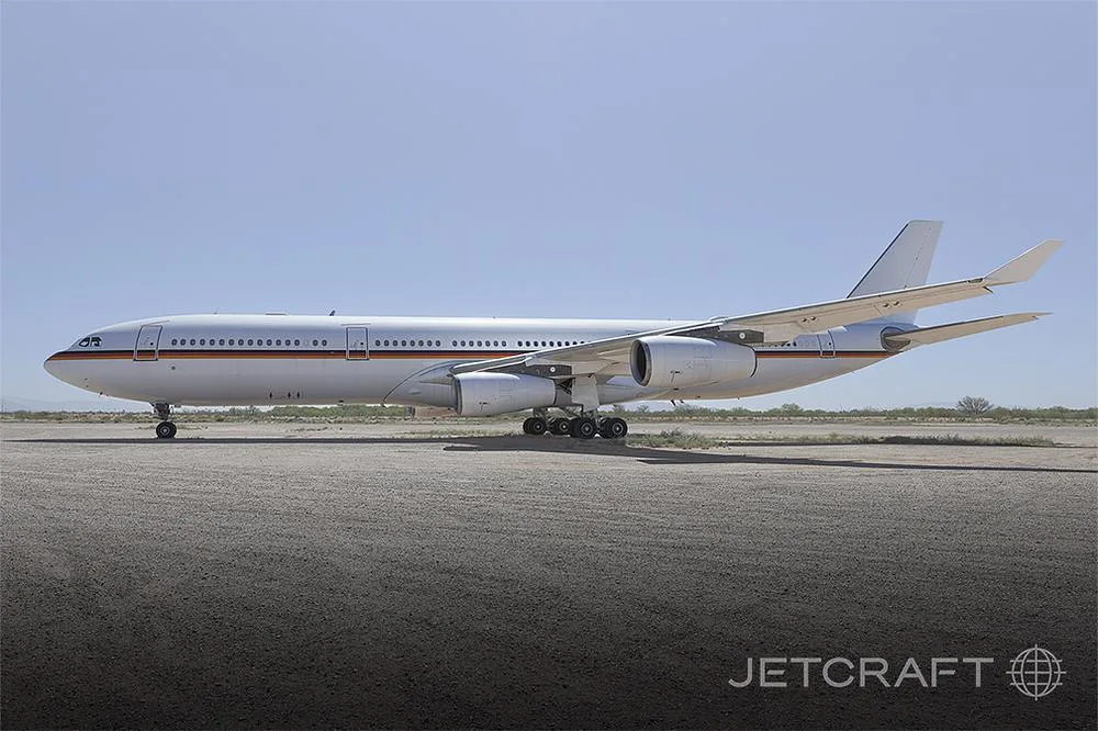 A side view of a white Airbus A340 aircraft with a German flag on the nose, parked on an asphalt surface under a clear sky.