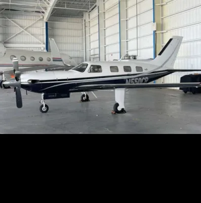 A silver and dark blue single-engine turboprop aircraft (N550CP) is parked in a hangar, with another jet visible in the background.