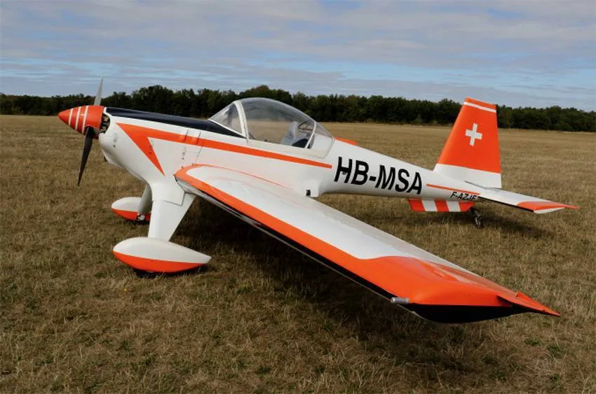 A white and orange single-engine sport aircraft with registration HB-MSA and a Swiss flag on the tail, parked on a grassy field.