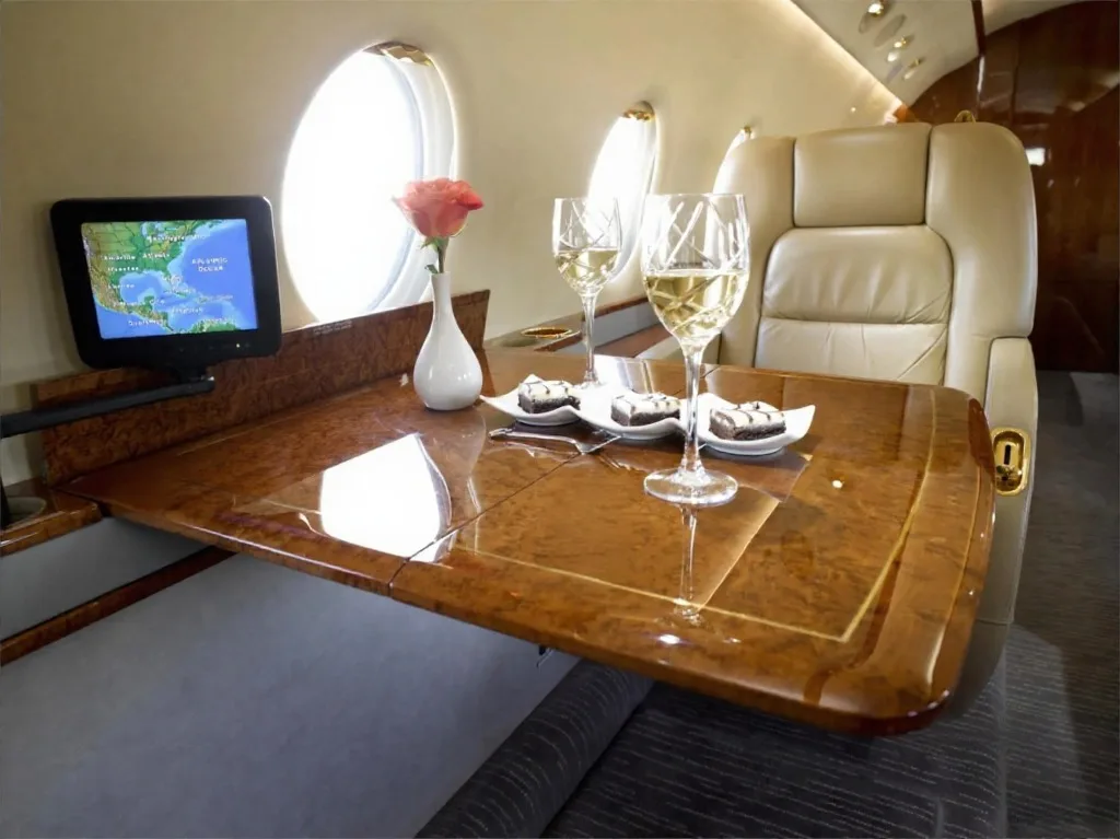 Interior view of the aircraft cabin with a table, wine glasses, and a monitor.