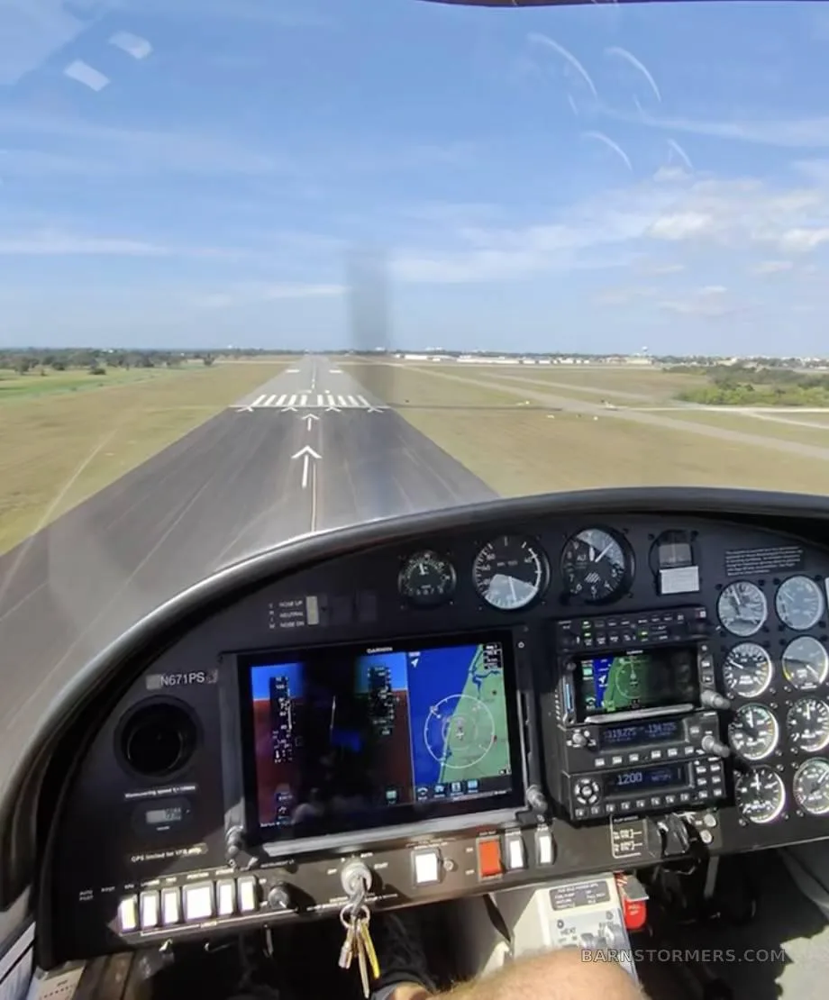 The cockpit of a Diamond DA20-C1 Eclipse, showing the instrument panel with Garmin displays and a runway visible through the windshield.