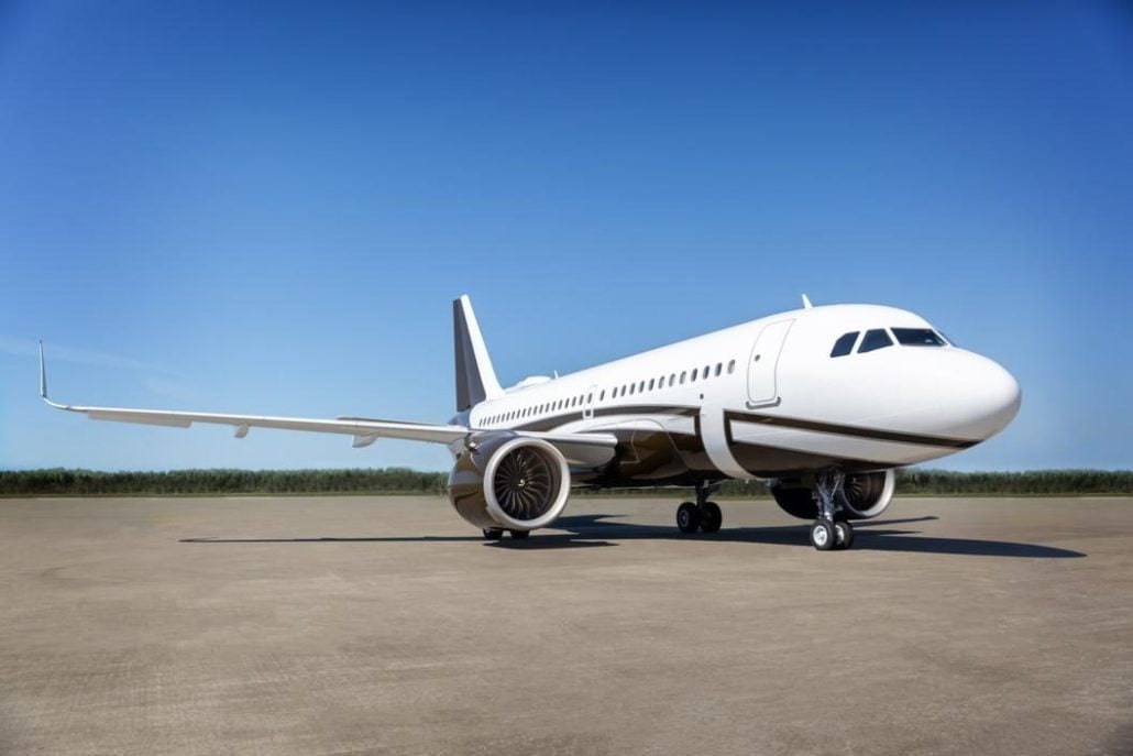 A white and dark grey Airbus A320 family aircraft parked on an empty tarmac under a clear blue sky.