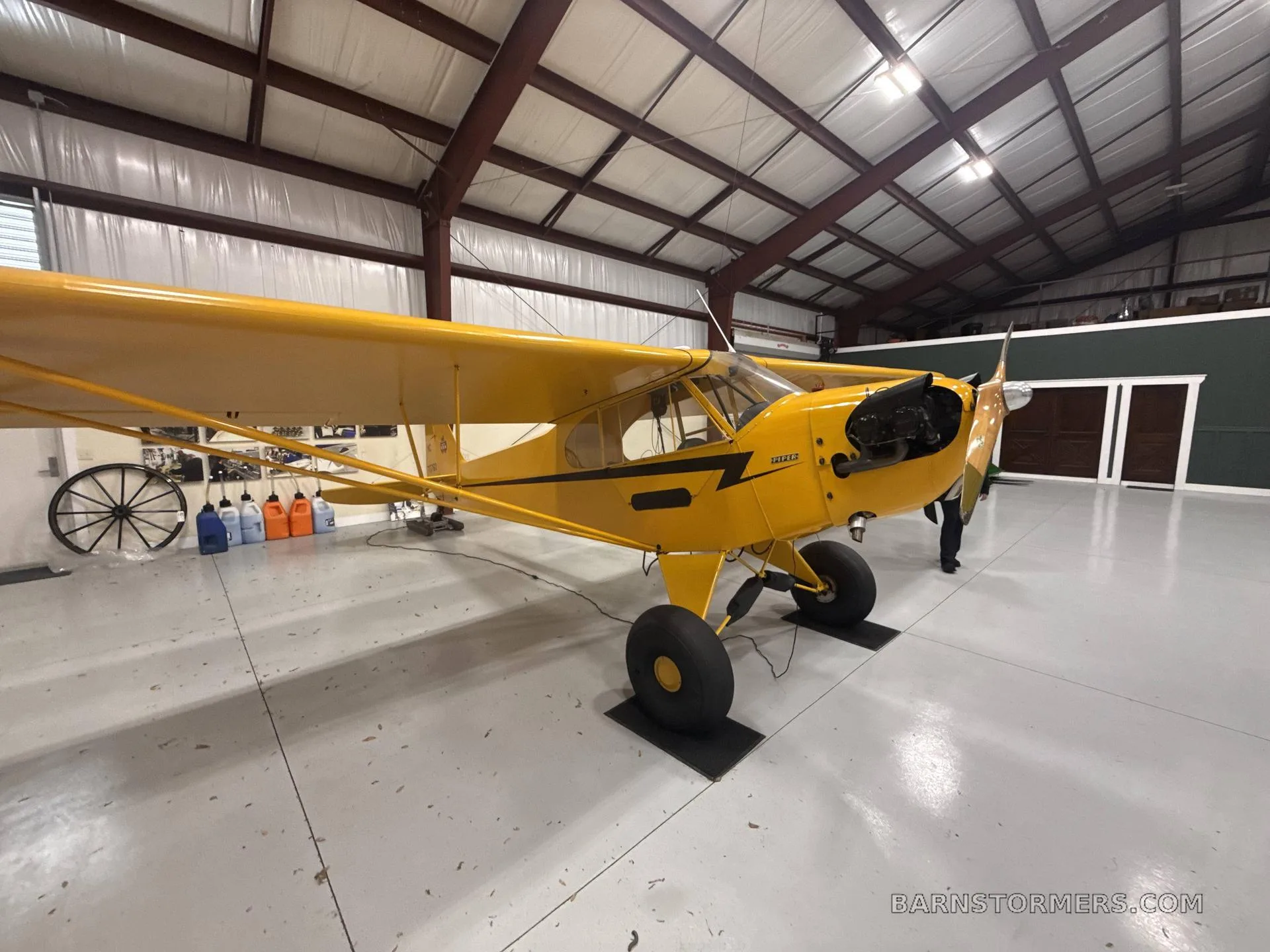 A yellow single-engine aircraft with its engine cowling open, parked inside a hangar.