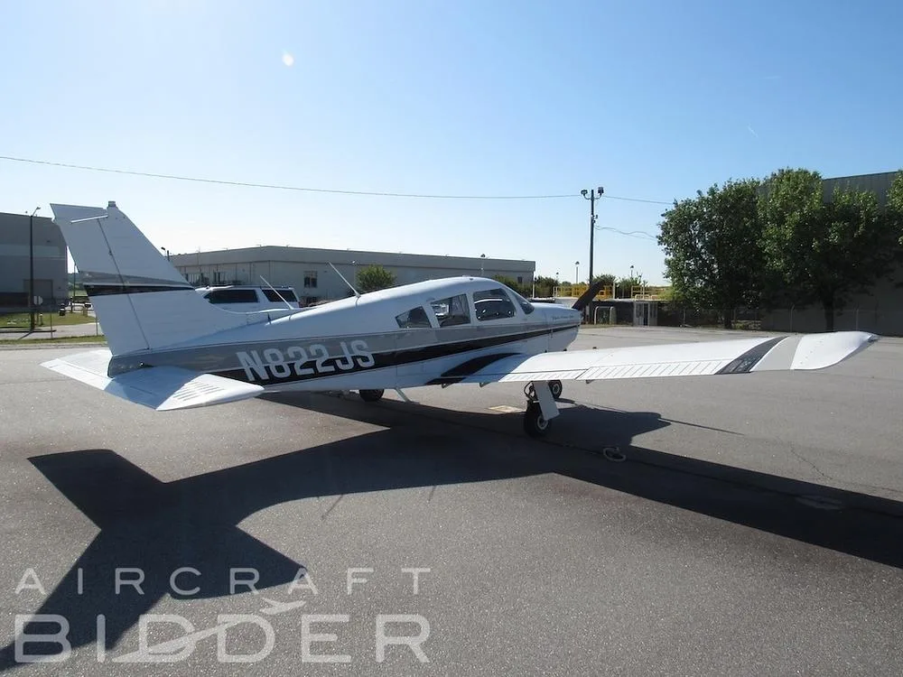 A rear-side view of the white Piper Arrow 200 (N822JS) with black and grey stripes, parked on an asphalt tarmac.