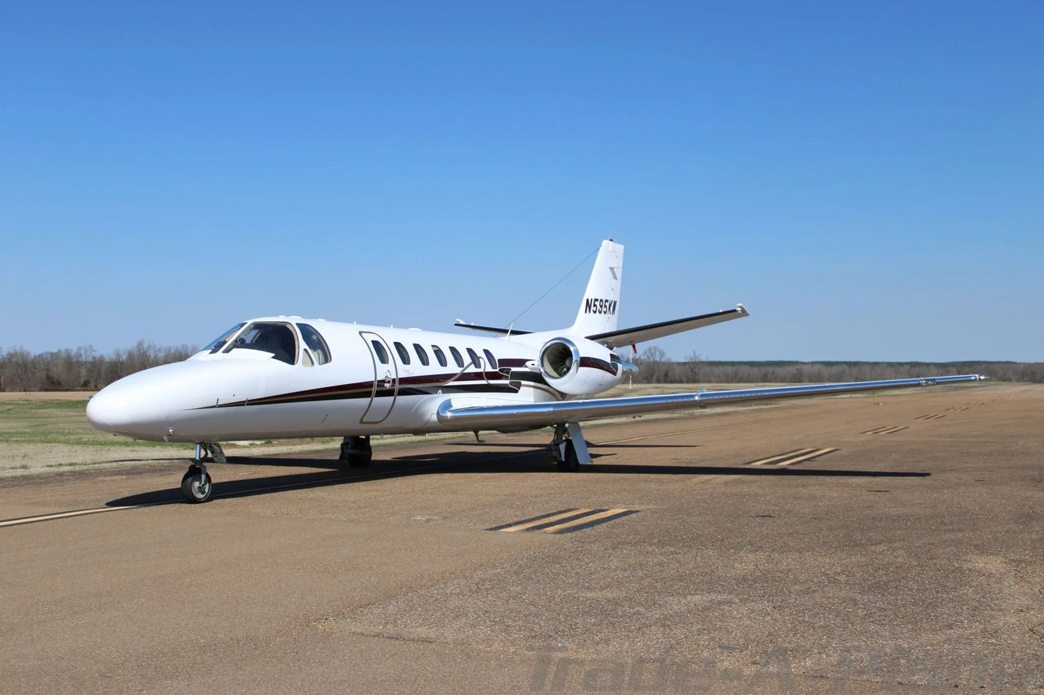 A three-quarter front view of a white Cessna Citation Encore business jet with dark brown and gold stripes on the tarmac.