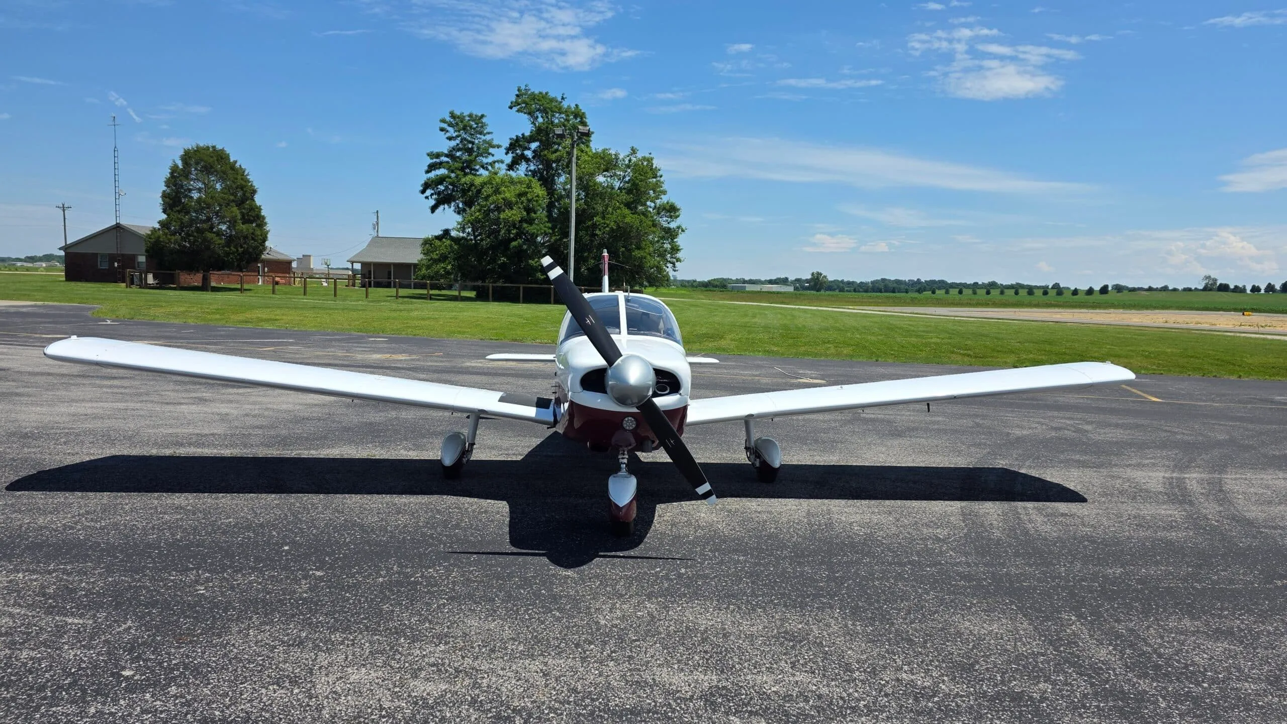 A head-on view of a white and maroon Piper Cherokee (N9221W) parked on an airfield.