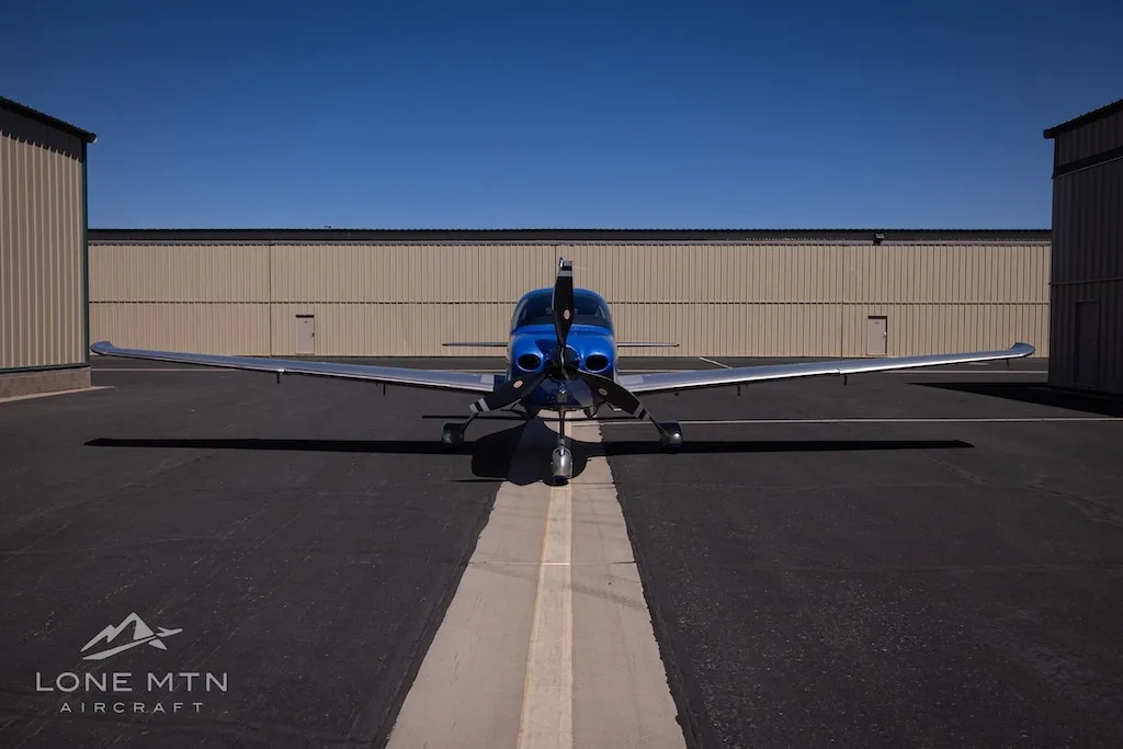 A head-on view of the blue and silver Cirrus SR22 aircraft, N365S, parked on an asphalt ramp between hangars.