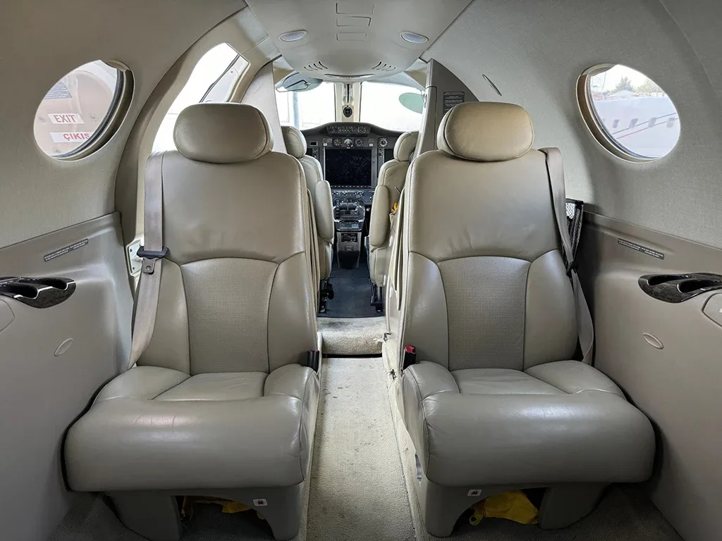 The interior cabin of a private jet with two rows of light brown leather seats, looking towards the cockpit.