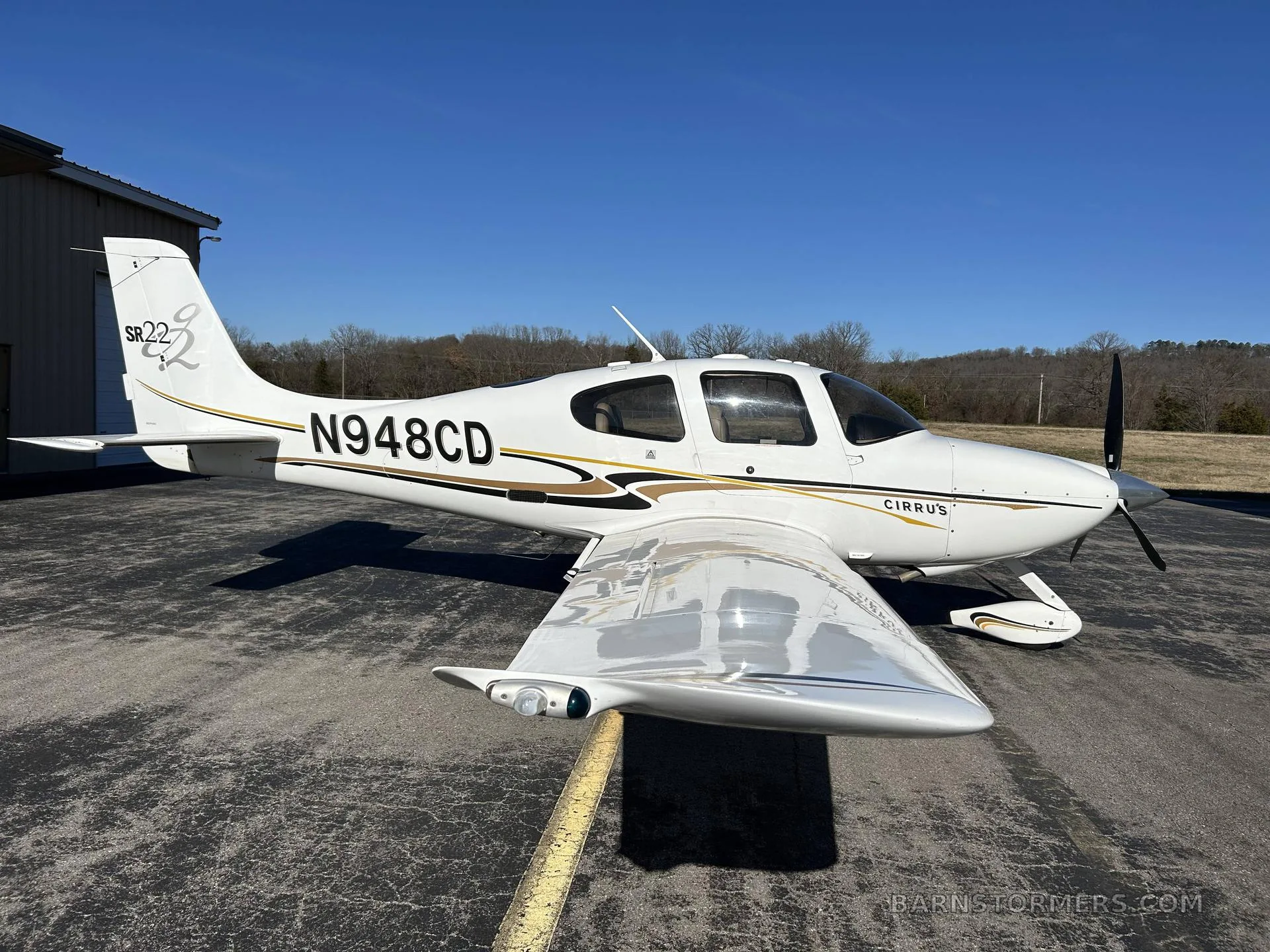 A white Cirrus SR22 aircraft with gold and black stripes, registration N948CD, parked on an asphalt ramp.