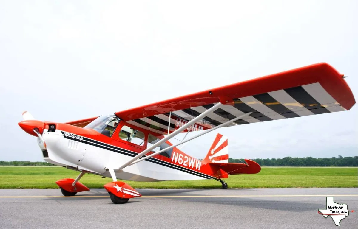 A red and white Super Decathlon aircraft with black stripes on the wings and a star pattern on the tail, parked on an airfield.
