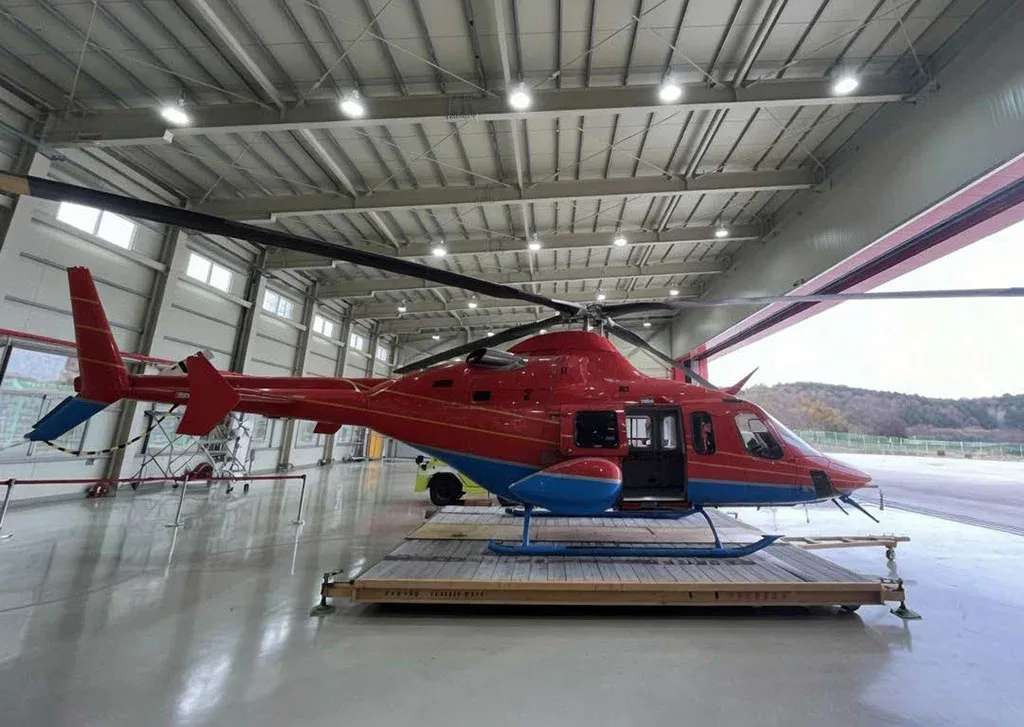 A red and blue helicopter with open doors sits on a platform inside a hangar.