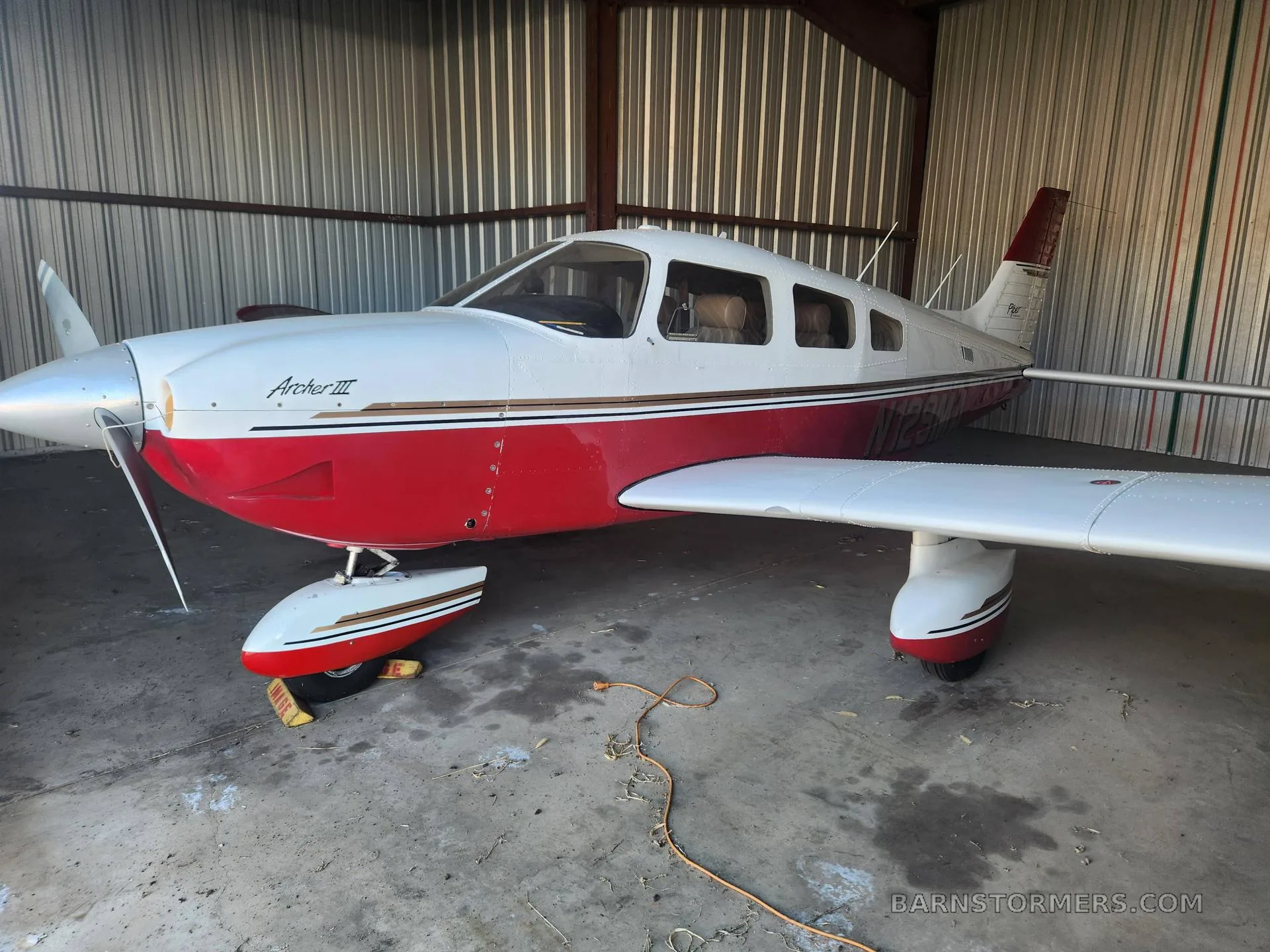A white and red Piper Archer III aircraft is parked inside a metal hangar.