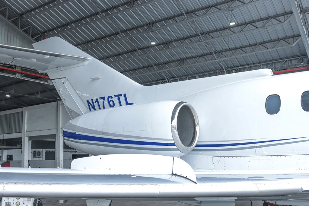 A close-up of the tail section of a white business jet with blue and grey stripes, showing registration N176TL.