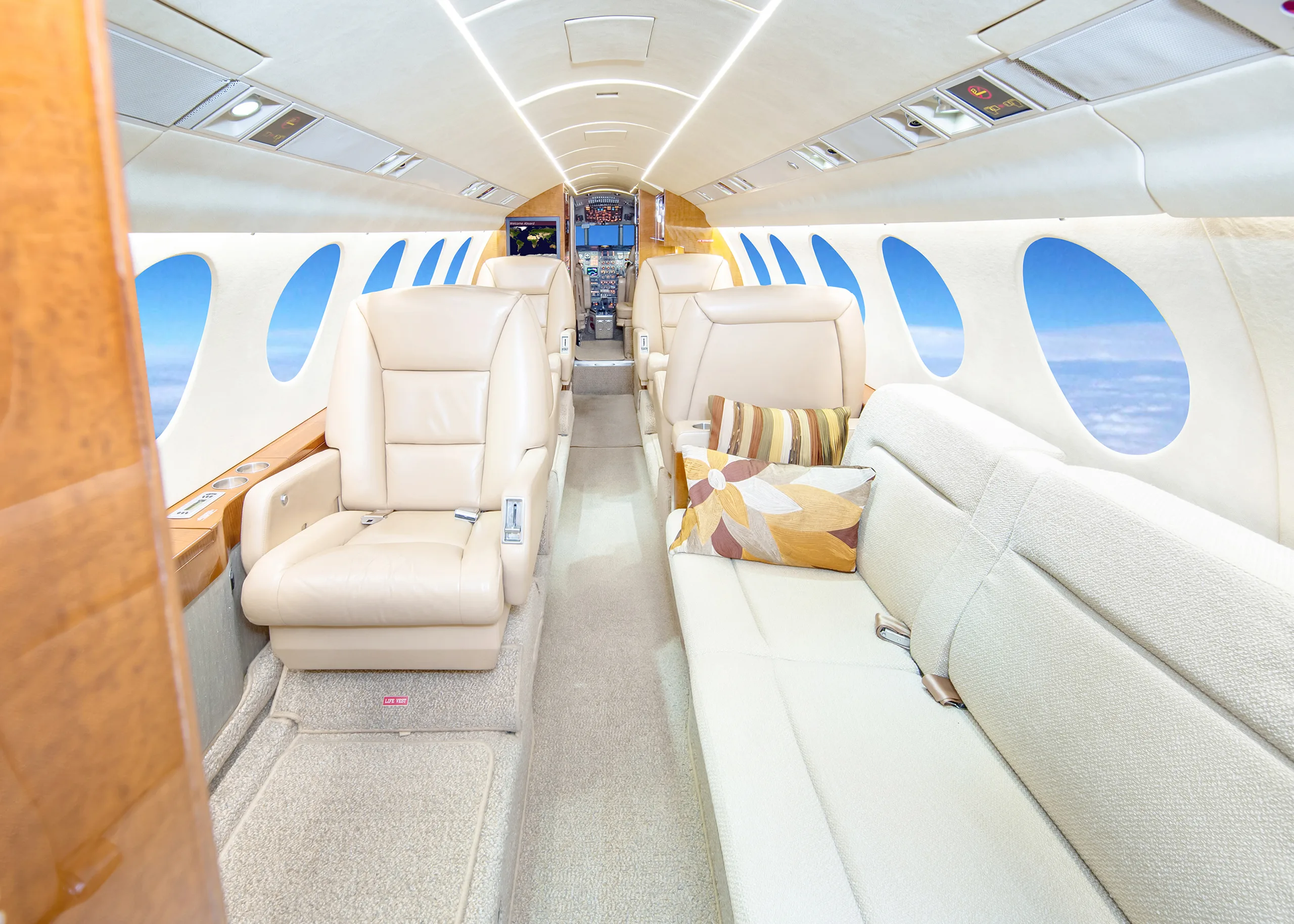 The luxurious interior of a private jet cabin with beige leather seats, a sofa, and windows showing blue sky.
