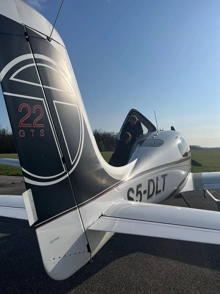 A rear view of the silver and white Cirrus SR22T aircraft S5-DLT, with people entering the cabin.