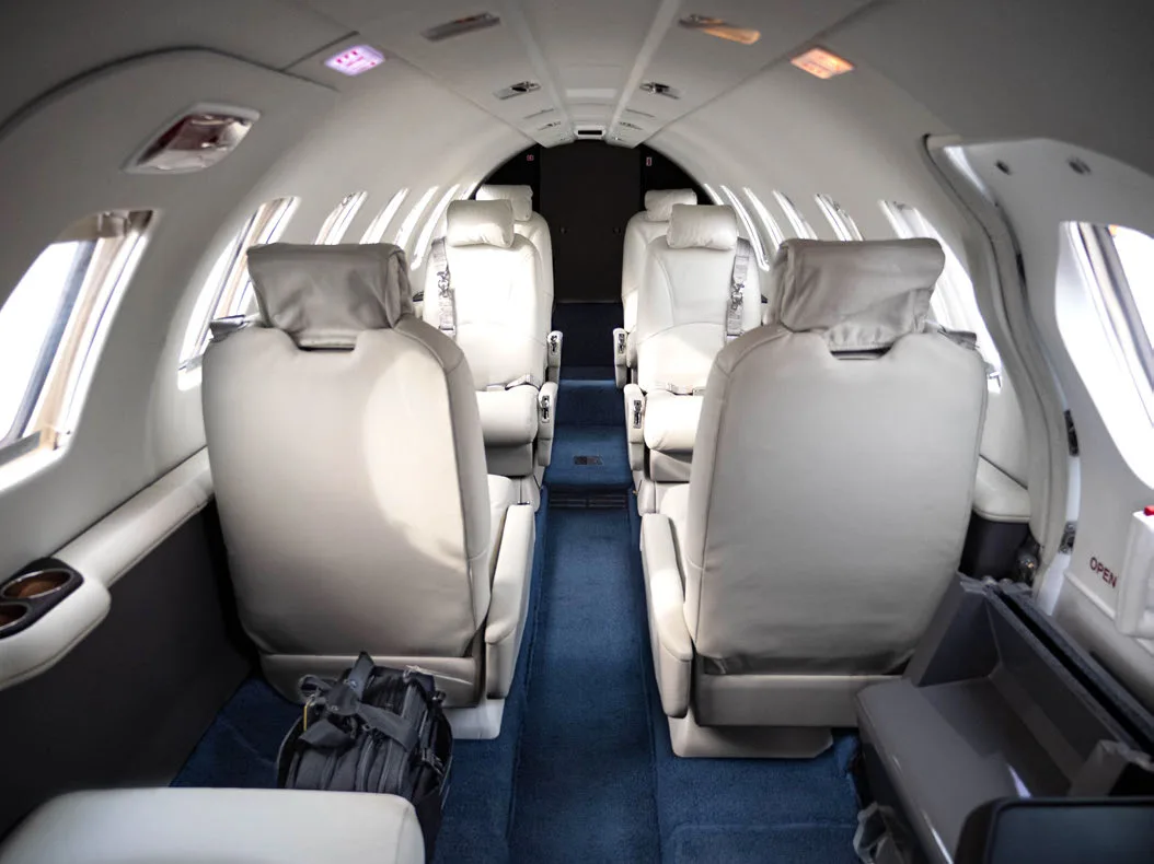 Aircraft interior with white leather seats and blue carpet.