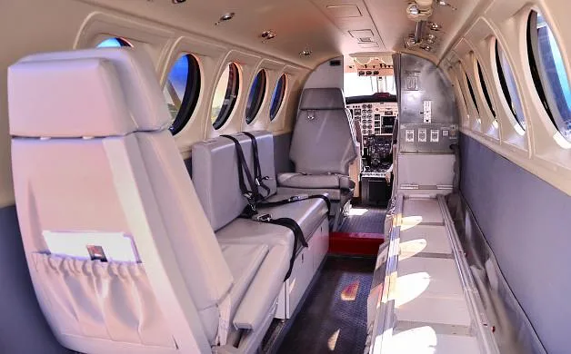 The interior cabin of the aircraft, featuring light gray seating and a view into the cockpit.
