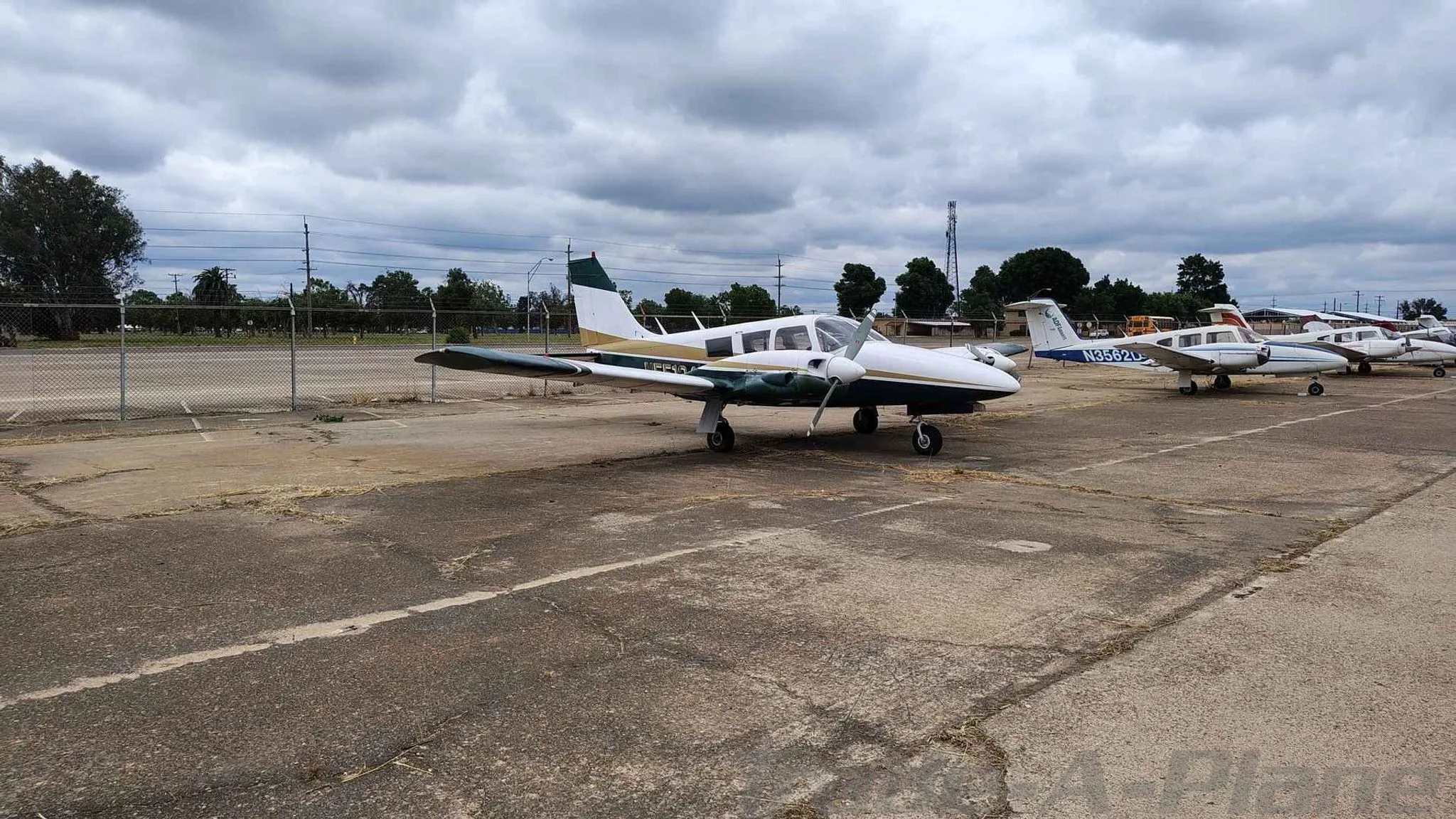 A side view of a white and green twin-engine Piper PA-23-200 aircraft parked on an asphalt lot.