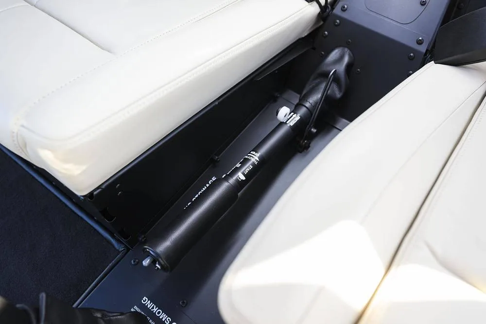 A close-up view of the floor between two light-colored seats in a helicopter, showing a control stick.