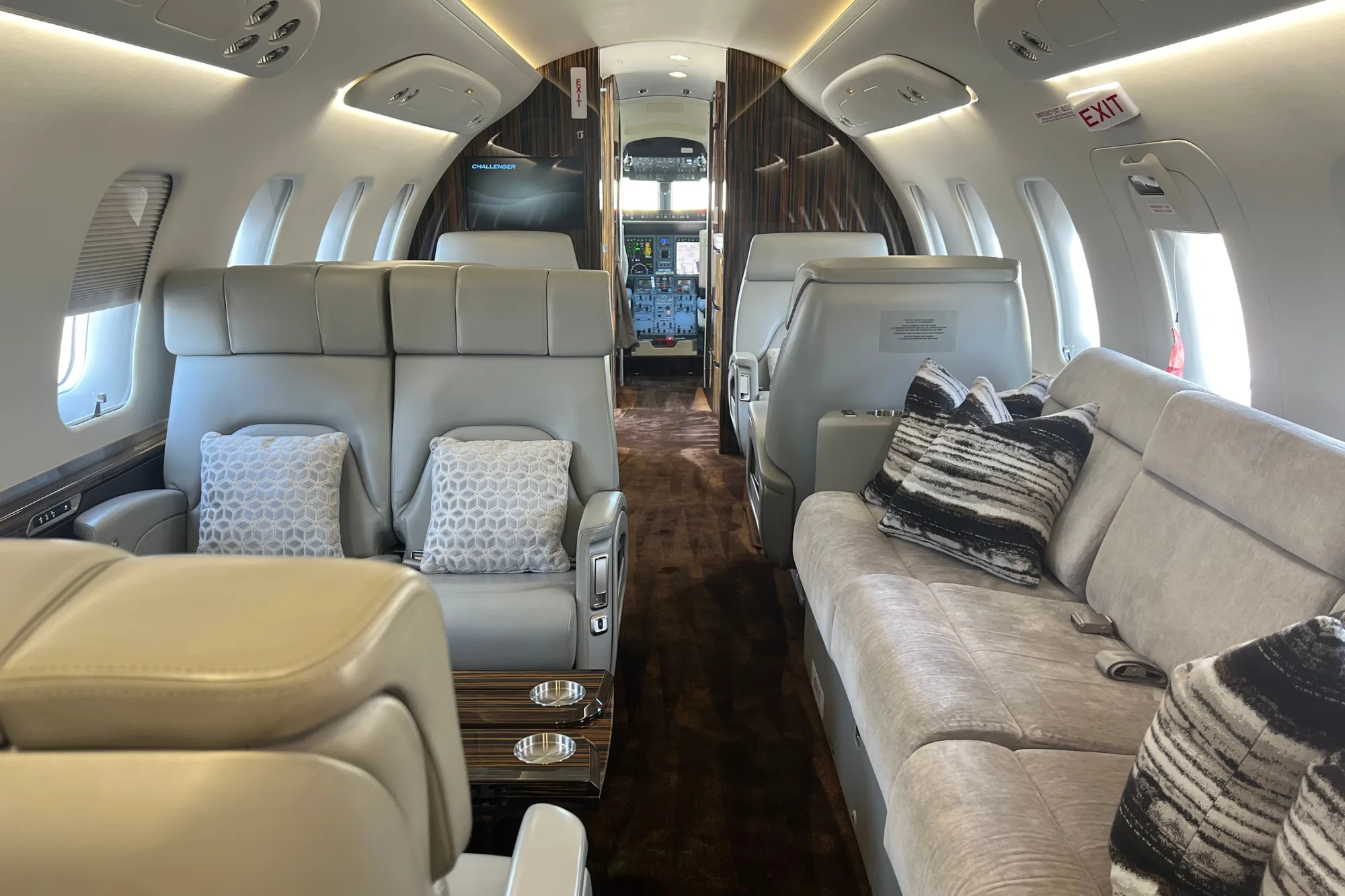 Luxurious aircraft cabin with light grey seats, a sofa, and cockpit visible.