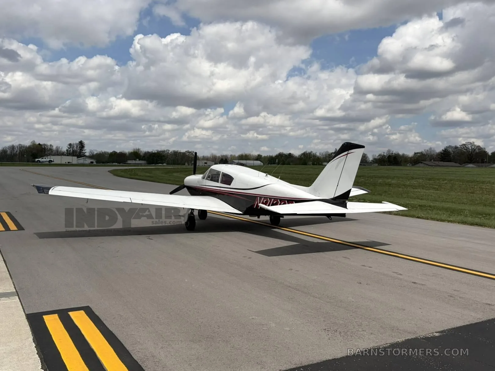 A white and black single-engine propeller aircraft with red accents, viewed from the rear-left, parked on an asphalt taxiway.