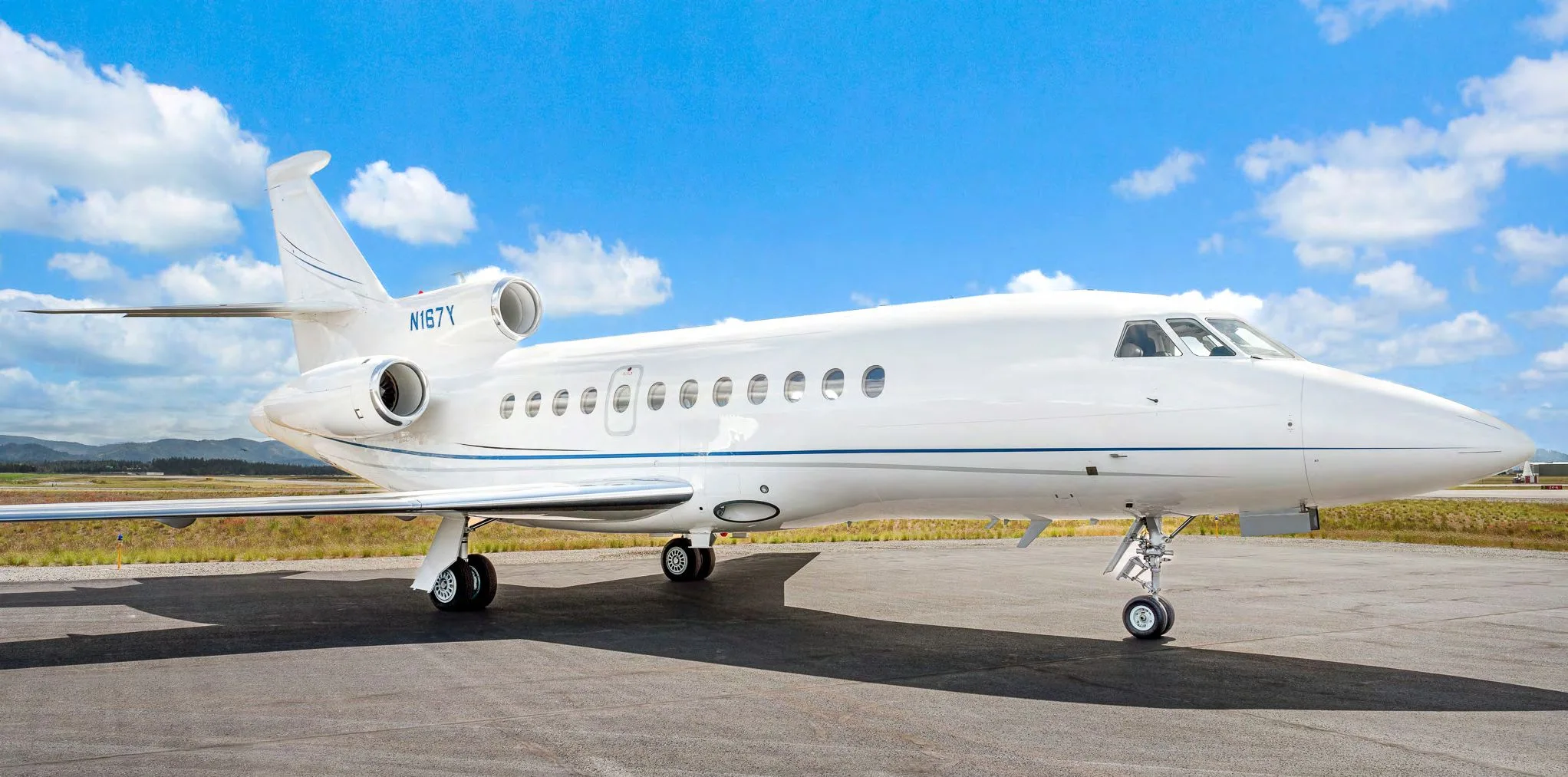 A white Dassault Falcon 900EX business jet, registration N167Y, parked on an airfield under a blue sky.