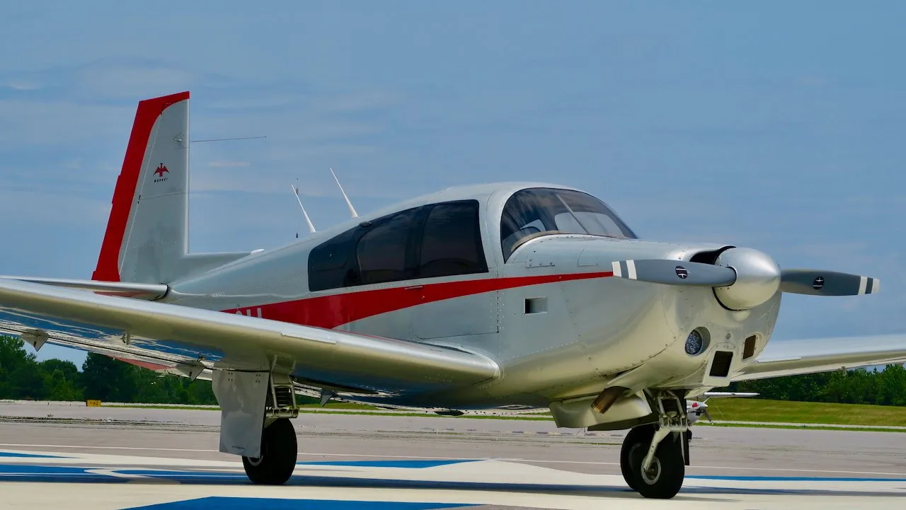Front-right view of a silver and red Mooney aircraft on an airfield.