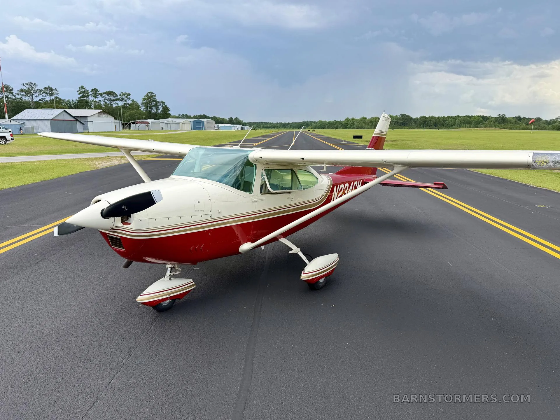 A red and white single-engine high-wing aircraft with registration N234CM is parked on an asphalt runway under a cloudy sky.