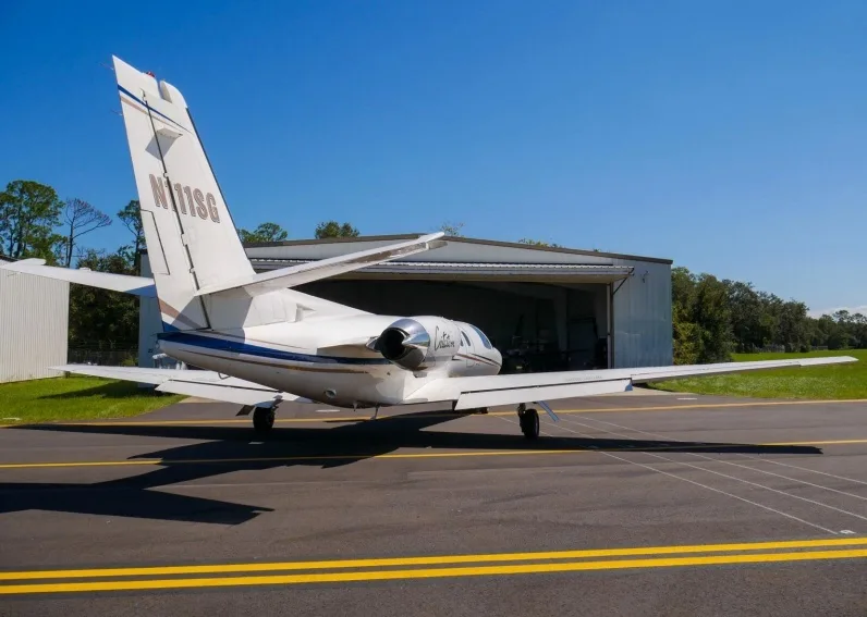 A rear view of a white Cessna Citation business jet, registration N111SG, parked on an asphalt runway in front of an open hangar.