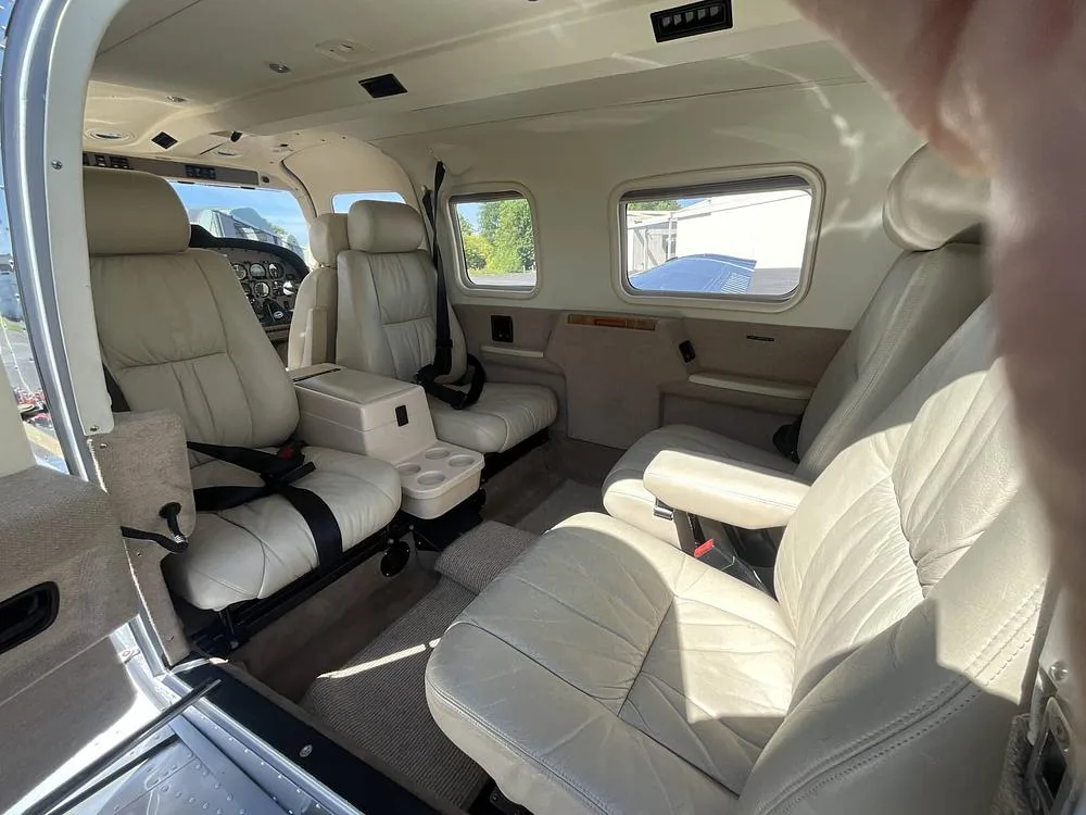 The beige leather interior cabin of a Piper Saratoga, showing passenger seating and windows.