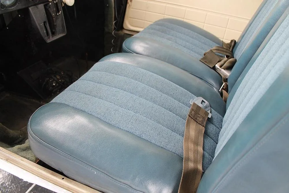 Close-up view of two blue fabric and vinyl aircraft seats with seatbelts.