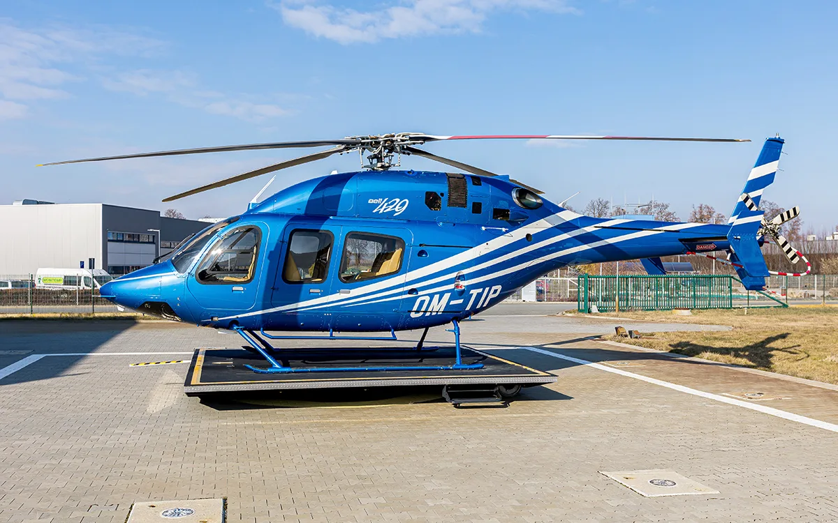 A blue Bell 429 helicopter with white and light blue stripes is parked on a helipad under a clear sky.